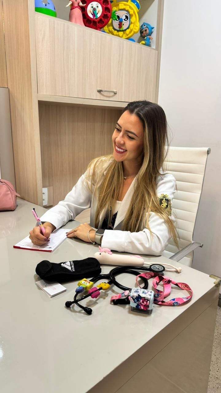 Dra Ana Karolina sorrindo e escrevendo no consultório